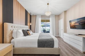 A modern bedroom with a large bed, a television, and a view of the outdoors. - 5BR Disney-area home | Pool, theater, themed (Kissimmee)