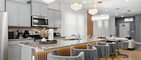 A modern kitchen with a central island, bar stools, a microwave, and a refrigerator.