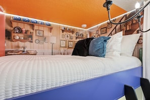 Quarto com cama, mesa de cabeceira, luminária e decorações nas paredes.