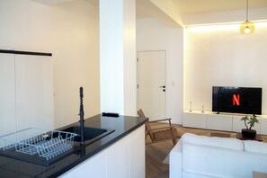 A modern living room with a flat-screen TV, a sofa, a dining area with a glass table, and a potted plant. - Brussels South - Cosy Appartment (Anderlecht (Brussels))