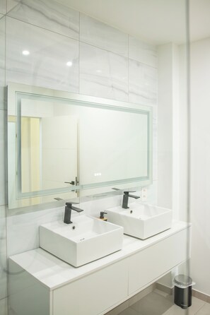A modern bathroom with two white sinks, a large mirror, and a trash can. - Brussels South - Cosy Appartment (Anderlecht (Brussels))