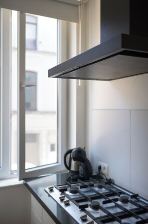 A kitchen with a gas stove, a window, and a black range hood. - Brussels South - Cosy Appartment (Anderlecht (Brussels))