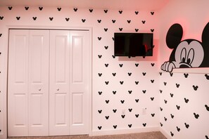 A room with a white door, a flat-screen TV mounted on the wall, and a Mickey Mouse decoration. - Themed 5BR near Disney | Pool, game room (Kissimmee)