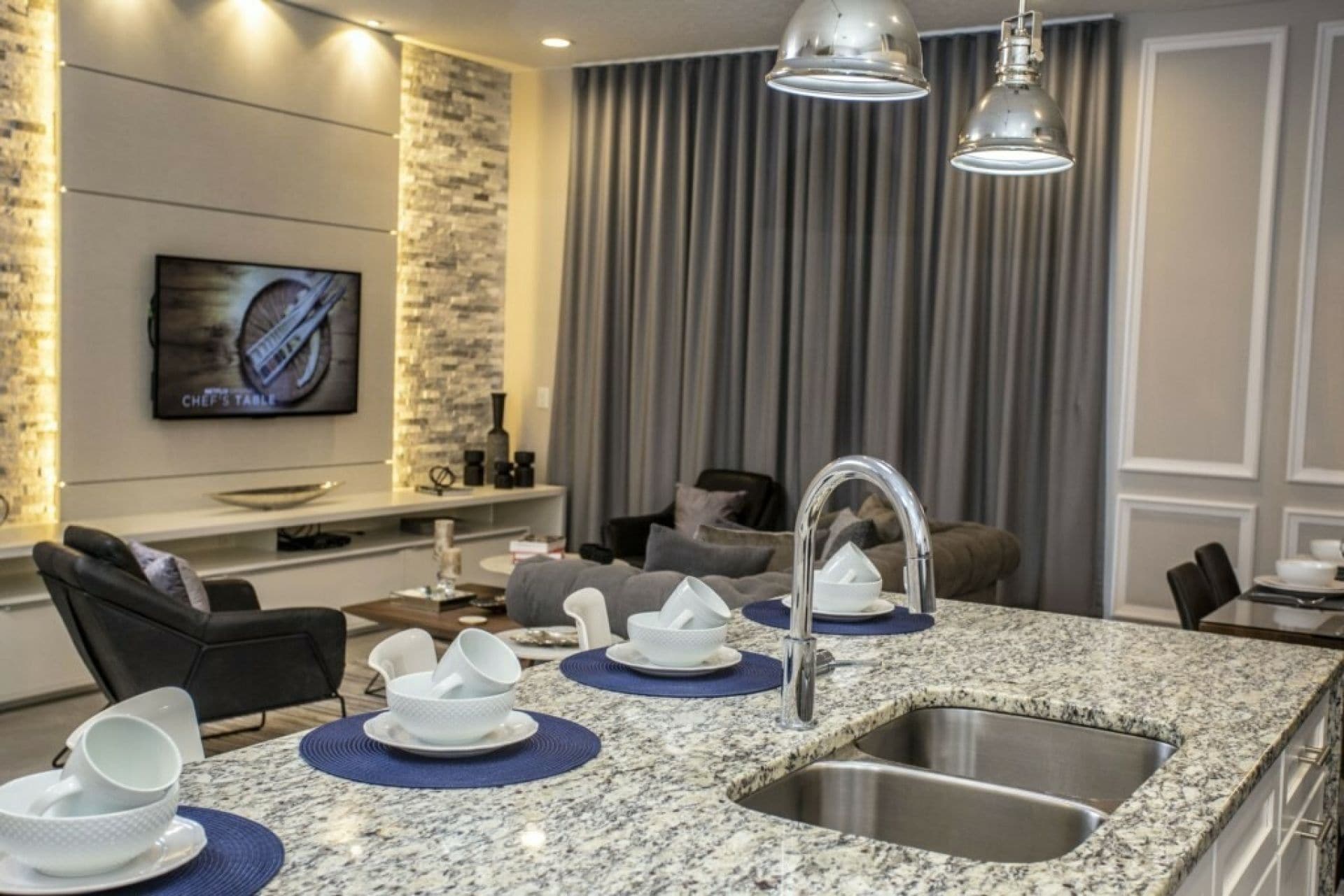 A modern kitchen with granite countertops, a stainless steel sink, and a dining area with a television.