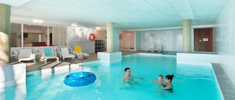 An indoor swimming pool with clear water, lounge chairs, and a lifebuoy on the wall.