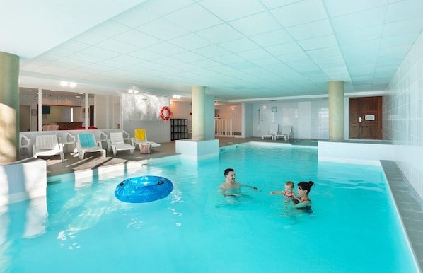 An indoor swimming pool with clear water, lounge chairs, and a lifebuoy on the wall.