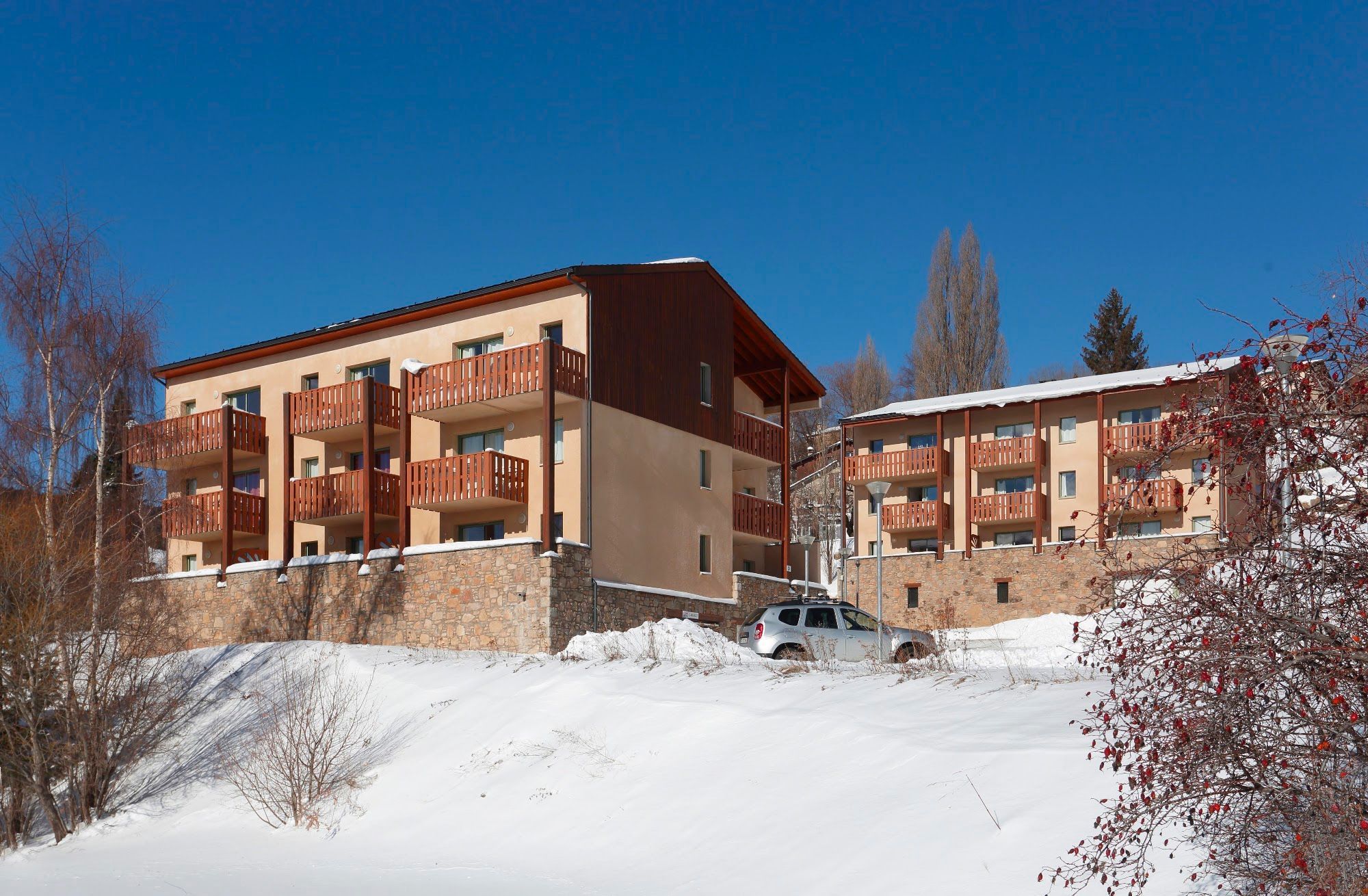 Een hotel met meerdere verdiepingen, balkons, een gevel van natuursteen en een met sneeuw bedekte grond.