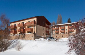 Ein mehrstöckiges Hotel mit Balkonen, einer Stein-Fassade und einem schneebedeckten Gelände.