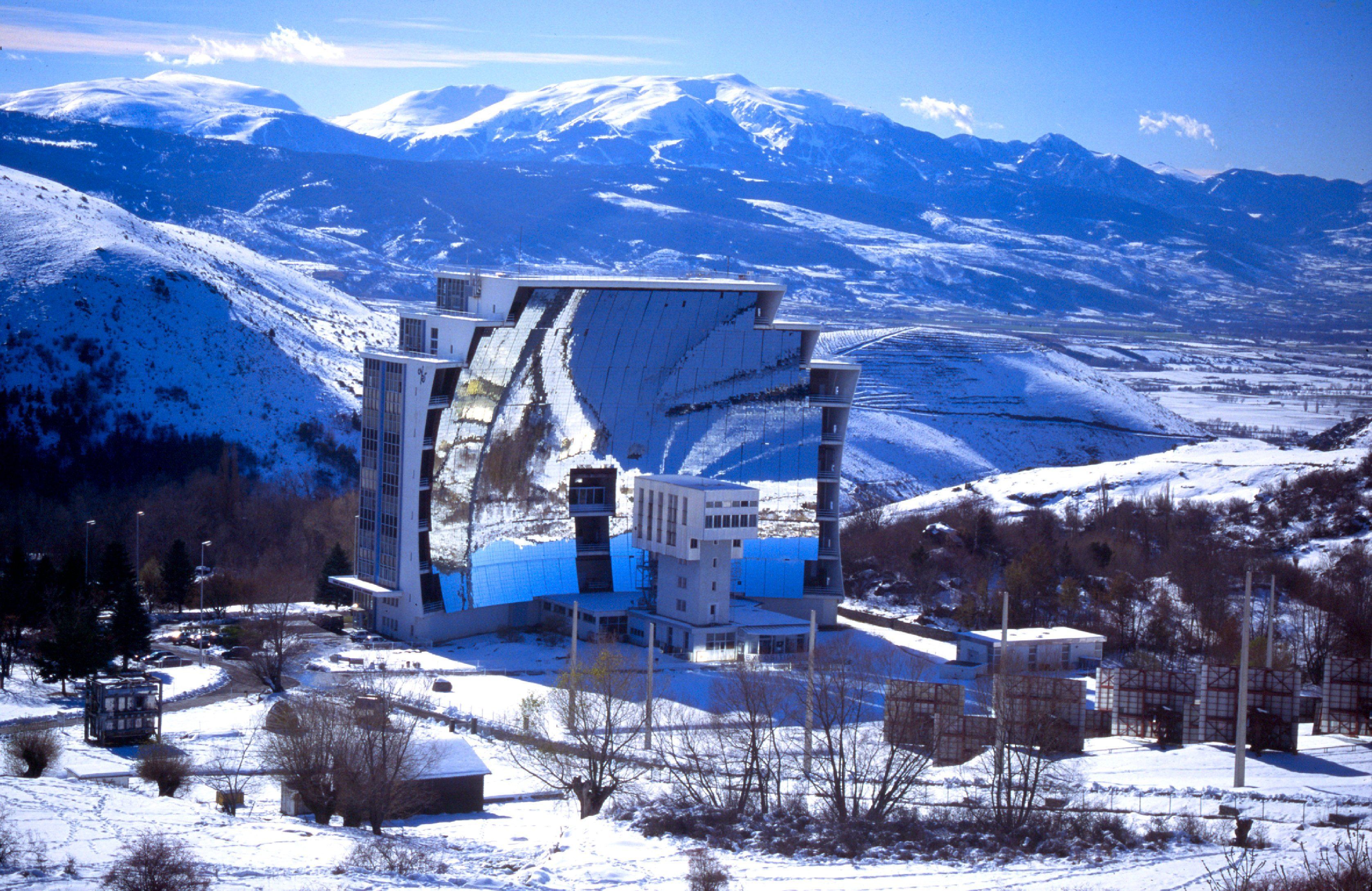 A modern building with a unique architectural design, surrounded by a snowy landscape and mountains in the background.
