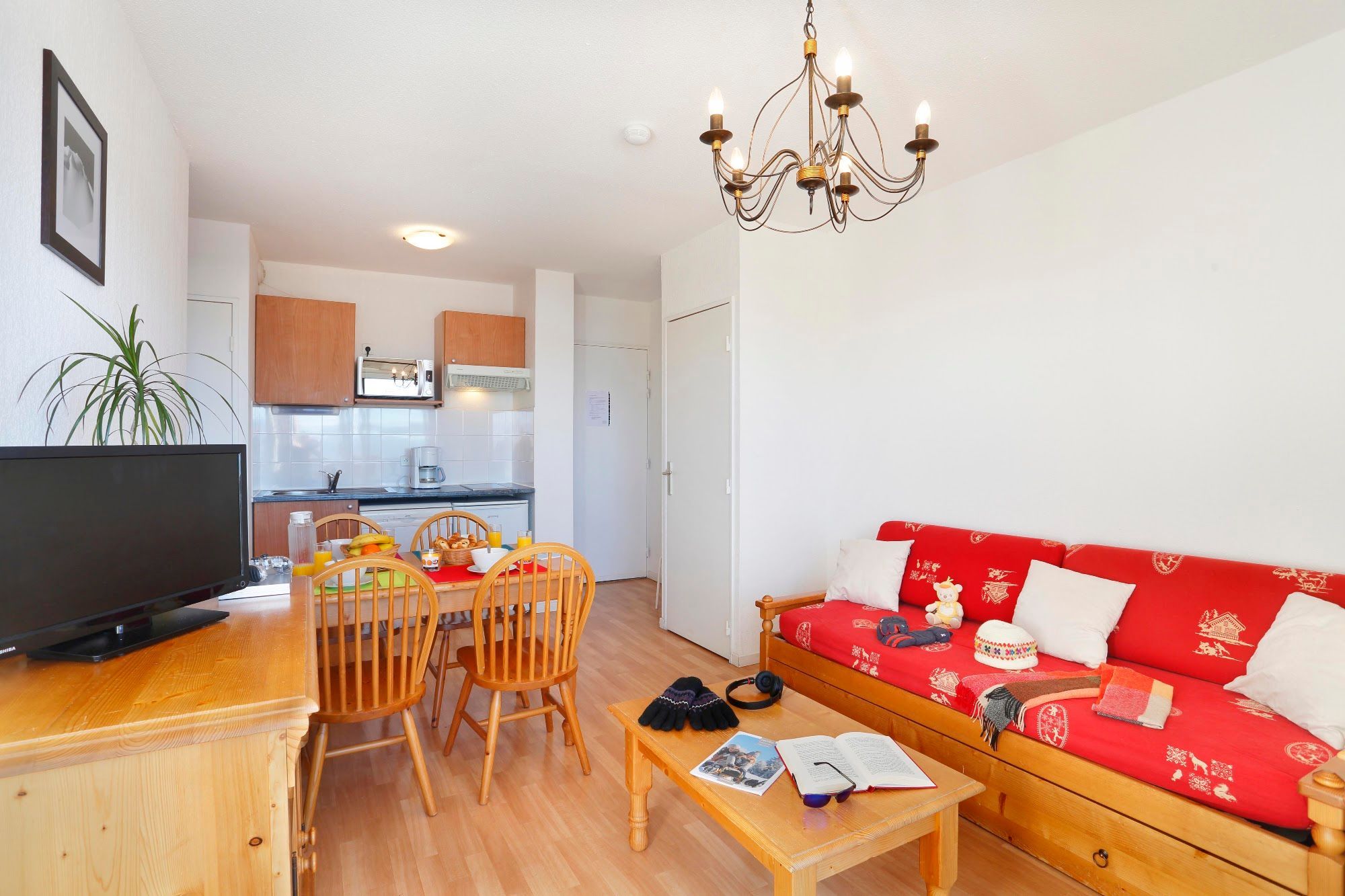 Een woonkamer met een rode bank, houten stoelen, een salontafel, een televisie en een kroonluchter.