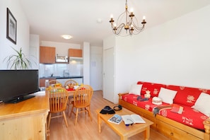 Ein Wohnzimmer mit einem roten Sofa, Holzstühlen, einem Couchtisch, einem Fernseher und einer Chandelier.