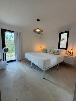 A bedroom with a bed, a bedside table with a lamp, a ceiling fan, and a window with curtains. - Hillside sanctuary with pool & sunset sea views. (Los Chivos)