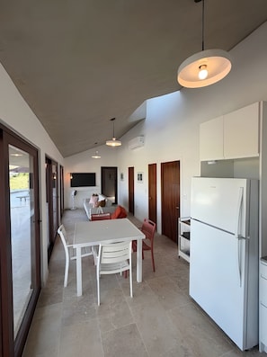 A modern kitchen with a dining area, a refrigerator, and a TV mounted on the wall. - Hillside sanctuary with pool & sunset sea views. (Los Chivos)