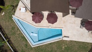 An aerial view of a swimming pool with a curved edge, surrounded by a patio area with outdoor furniture and umbrellas. - Hillside sanctuary with pool & sunset sea views. (Los Chivos)