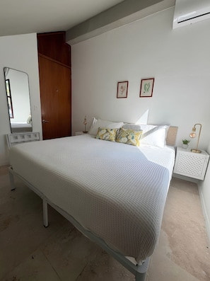 A bedroom with a bed, a wooden wardrobe, a bedside table with a lamp, and a wall-mounted air conditioner. - Hillside sanctuary with pool & sunset sea views. (Los Chivos)