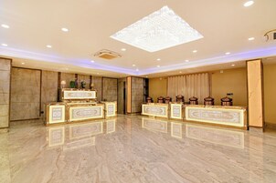 Un amplio vestíbulo de hotel con suelo de mármol, una gran araña de cristal y muebles ornamentados.