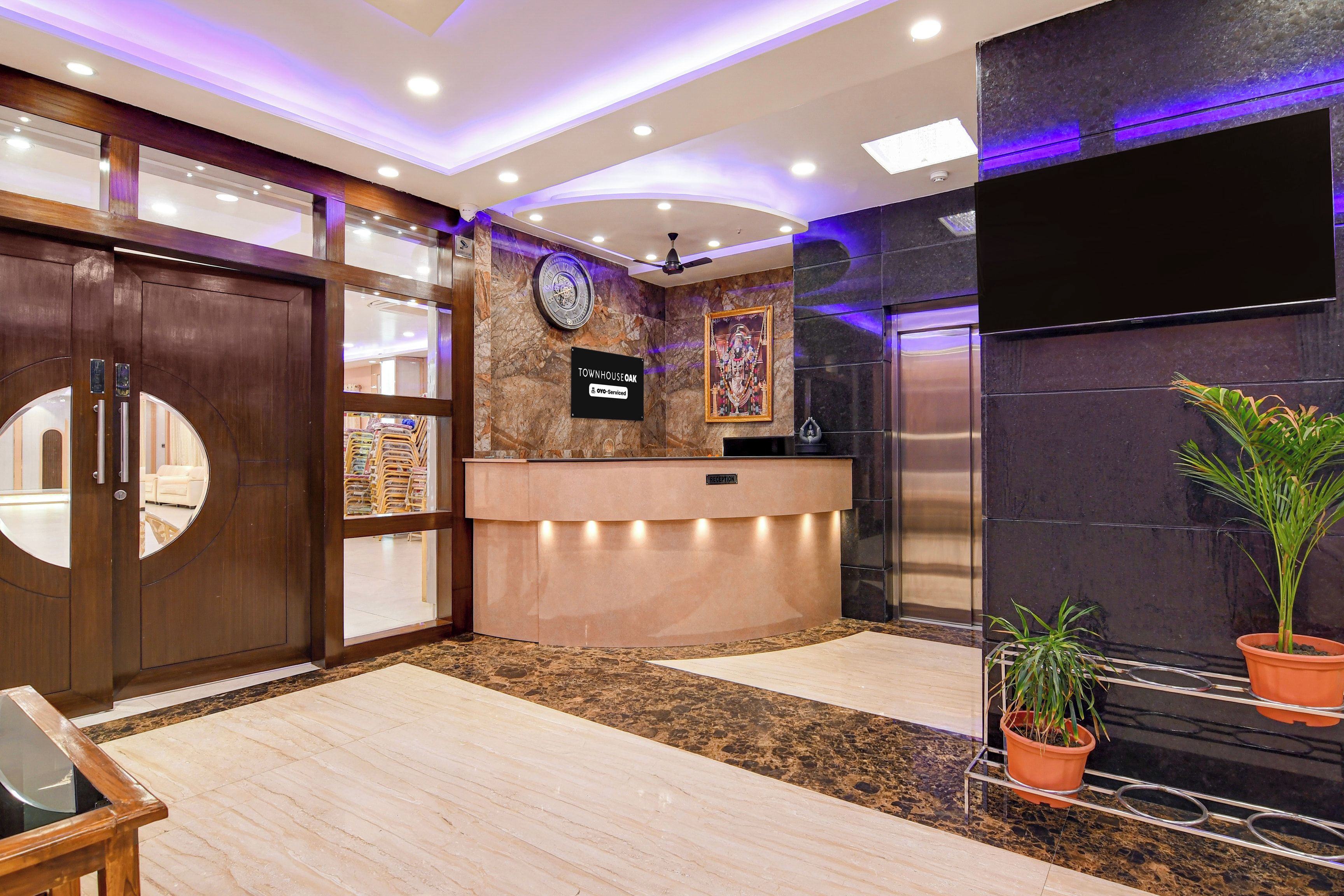 Ein Empfangsbereich mit Holztür, einer Rezeption, einer Uhr und einem Schild, das angibt, dass der Service von OVO übernommen wird.