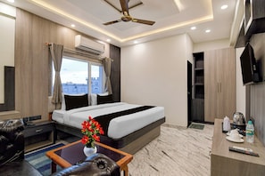 A hotel room with a bed, a desk, a chair, a coffee maker, a remote control, and a television.