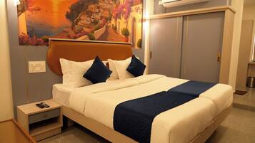 A hotel room with a bed, bedside table, nightstand, and a painting on the wall.