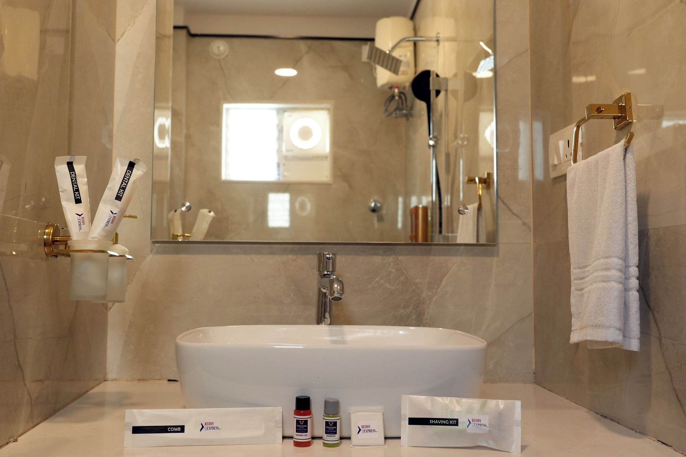 Un baño con lavamanos grande, espejo y artículos de aseo, incluyendo un kit de afeitar, gel de ducha y champú.