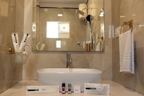 A bathroom with a large sink, mirror, and toiletries including a shaving kit, shower gel, and shampoo.
