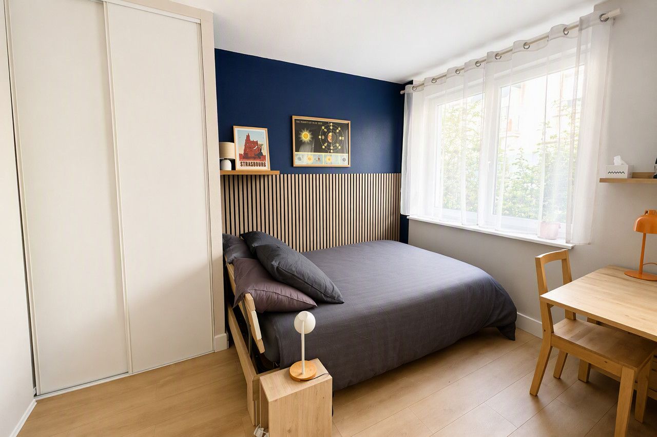 Une chambre à coucher avec un lit, une table de chevet, une lampe et une fenêtre avec des rideaux.