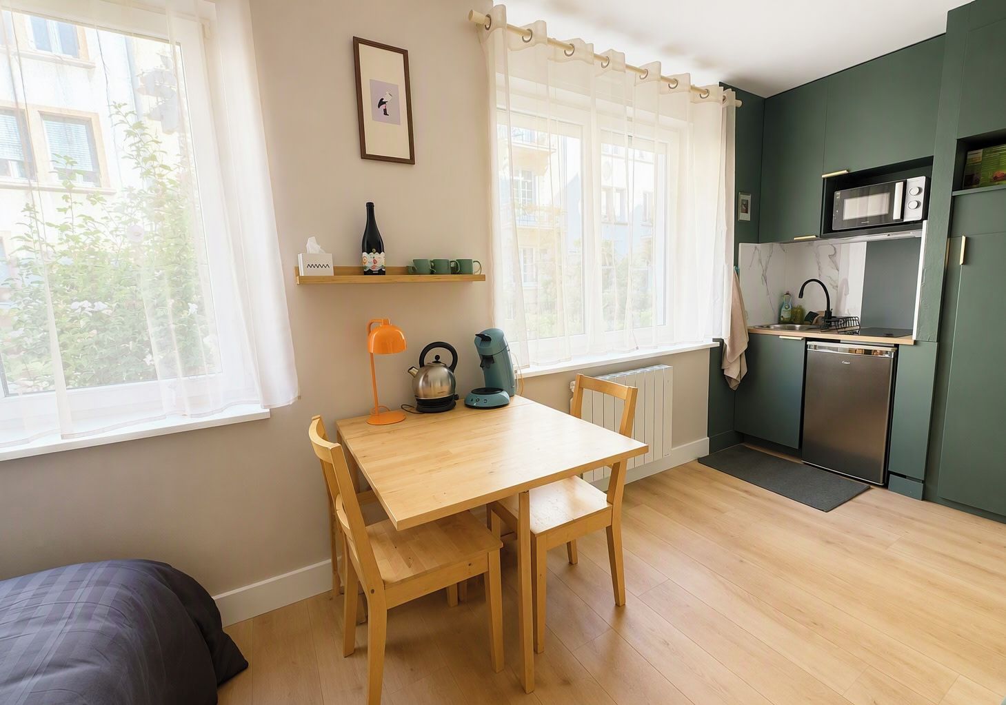Une cuisine compacte avec une table et des chaises en bois, une bouilloire, une machine à café et un four à micro-ondes.