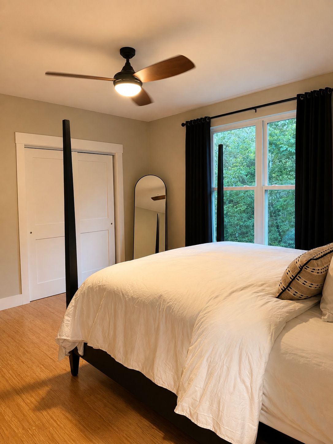 Quarto com cama, ventoinha no teto, janela com cortinas e porta.