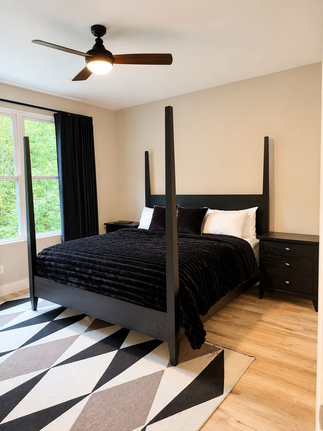 Een slaapkamer met een hemelbed, een plafondventilator, een nachtkastje en een raam met gordijnen.