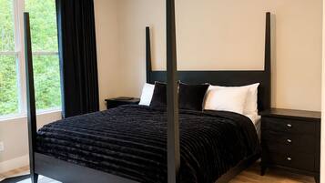 Een slaapkamer met een hemelbed, een plafondventilator, een nachtkastje en een raam met gordijnen.