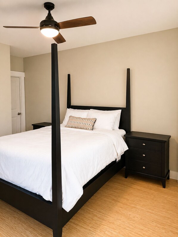 Uma cama com dossel, ventilador de teto, roupa de cama branca e mesa de cabeceira com gavetas.