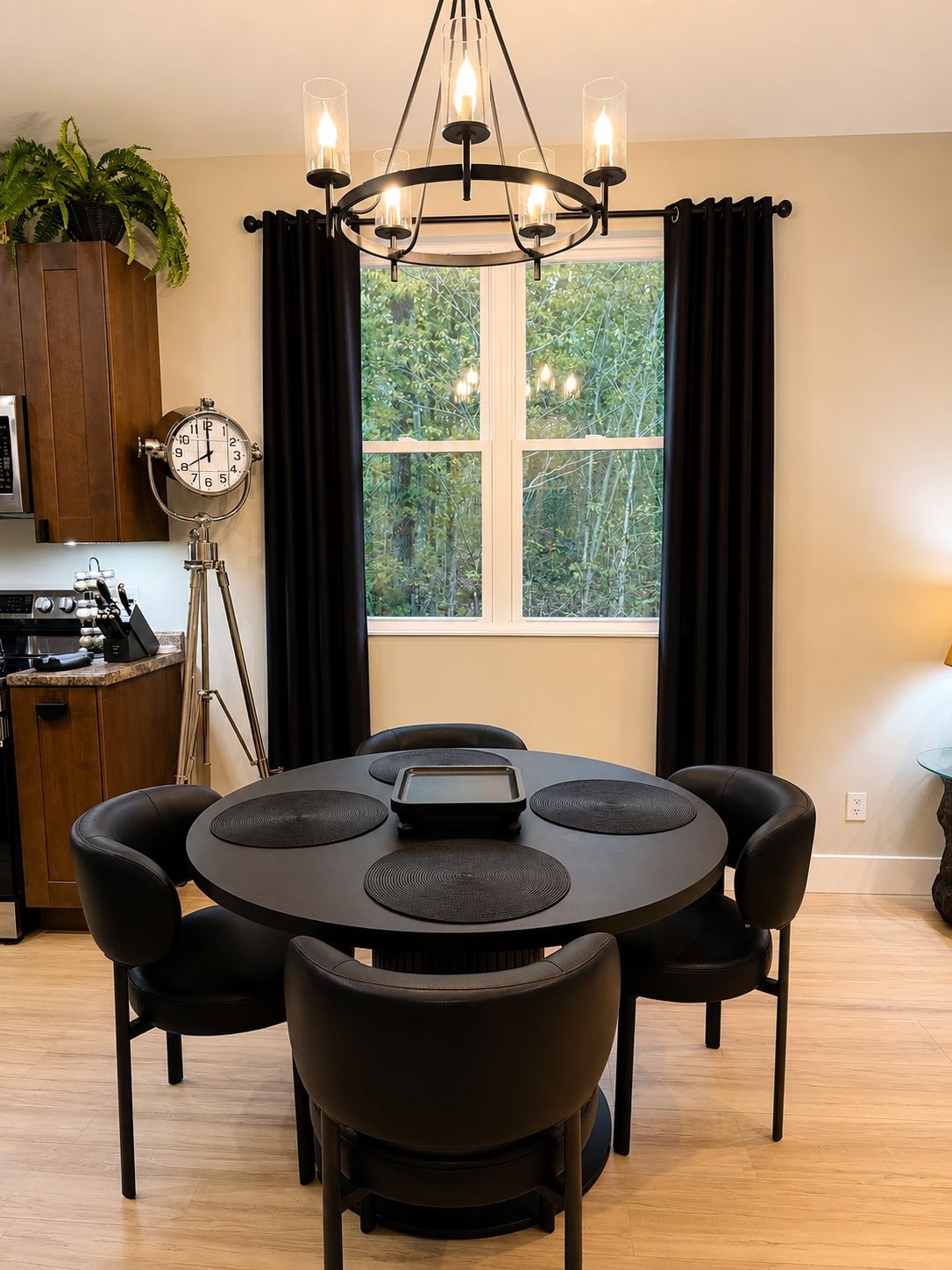 Ein Essbereich mit einem runden Tisch, schwarzen Stühlen, einer Chandelier, einer Uhr und einem Fenster mit Vorhängen.
