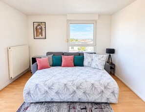 Une chambre à coucher avec un lit, un radiateur, une fenêtre, un tableau accroché au mur et une lampe sur une table de chevet.
