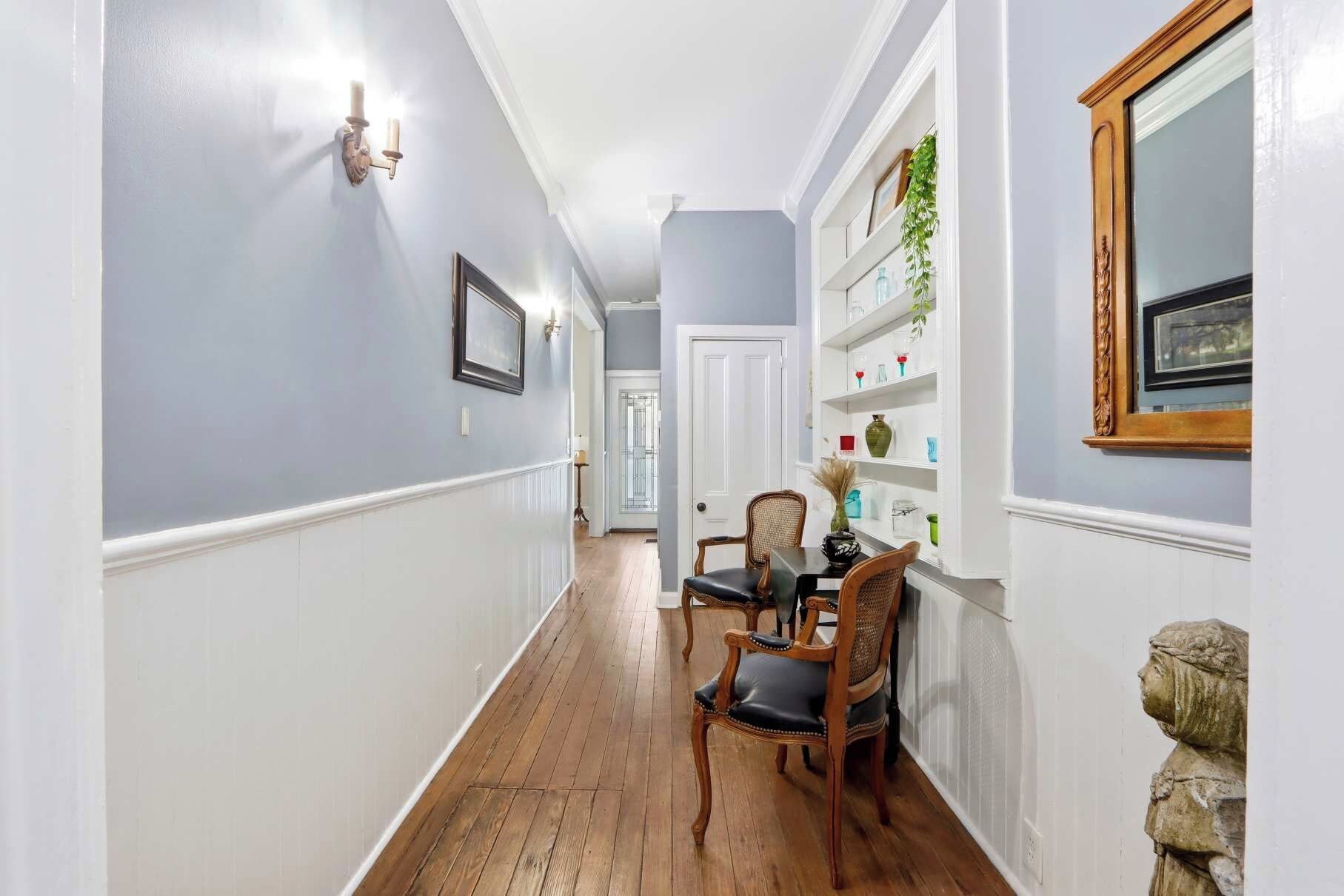 A hallway with wooden flooring, white walls, a door at the end, and a shelf with decorative items.