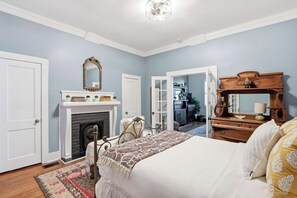 A bedroom with a bed, a dresser, a mirror, a fireplace, and a door leading to another room. - The Wrought Iron Place | Historic 1870 Savannah (Savannah)