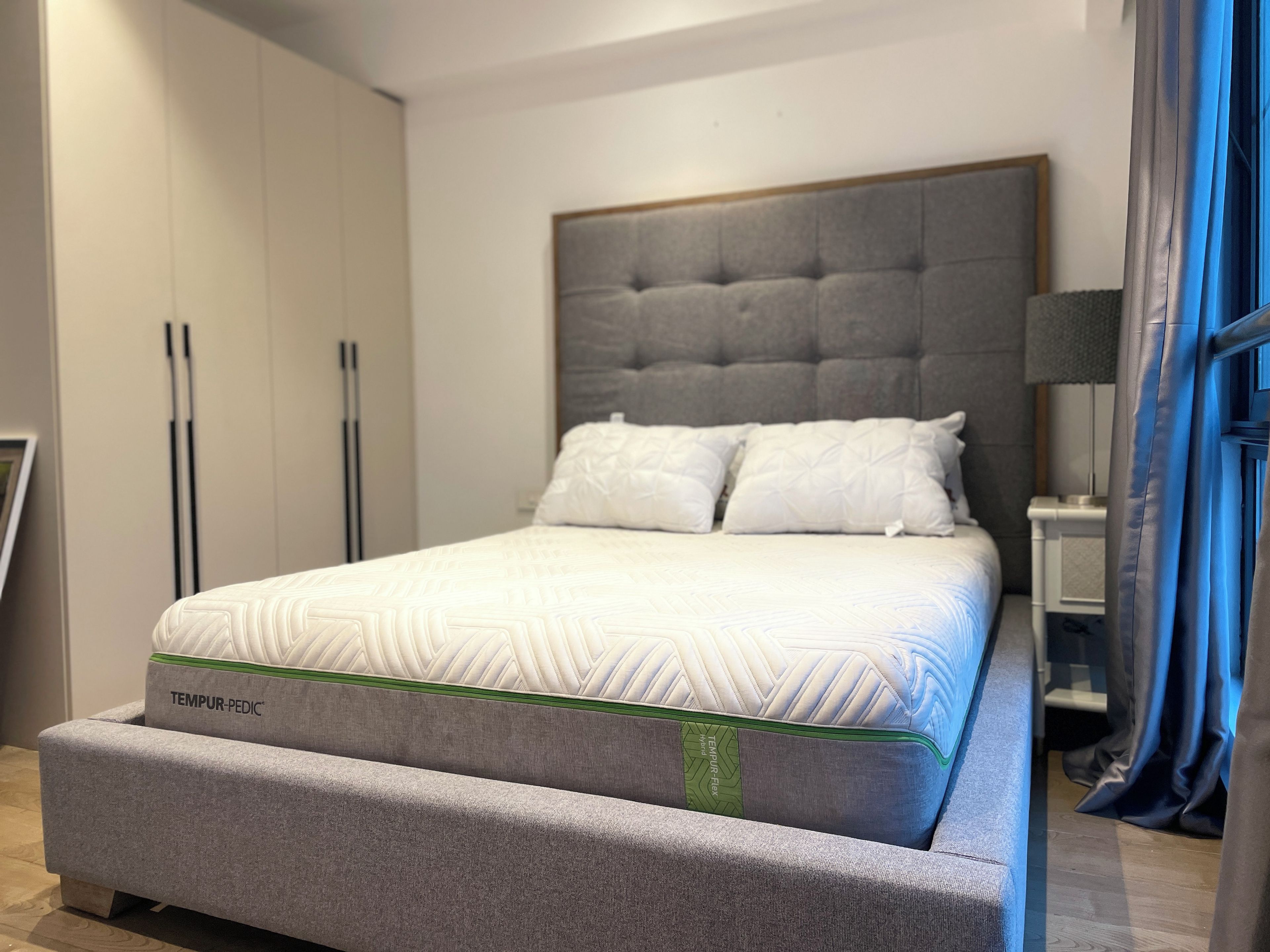 Een moderne slaapkamer met een groot bed, een grijs gestoffeerd hoofdeinde en een grijze slaapbank.