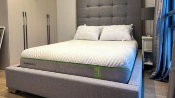 Een moderne slaapkamer met een groot bed, een grijs gestoffeerd hoofdeinde en een grijze slaapbank.
