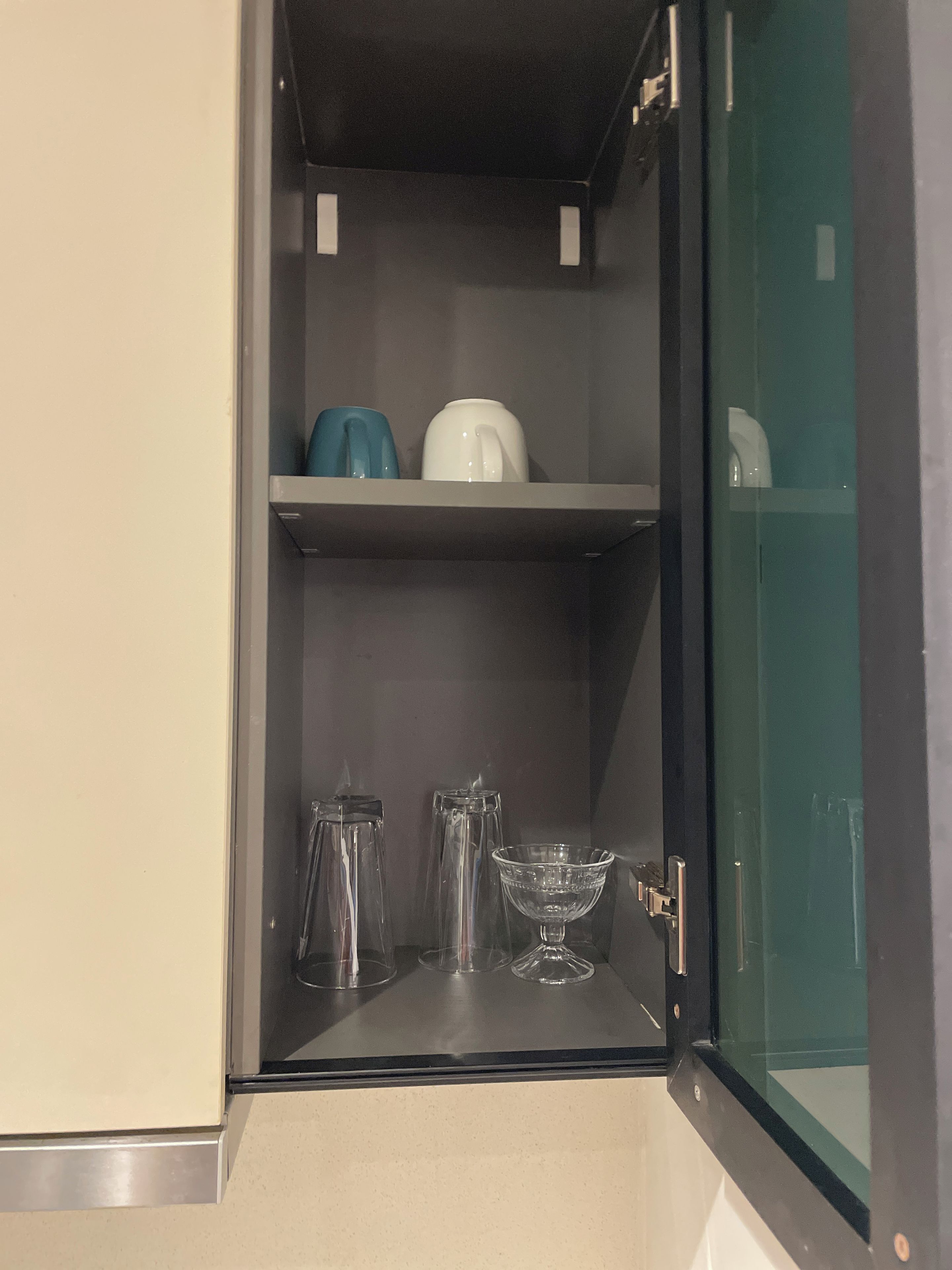 A kitchen with a built-in cabinet containing a kettle, a coffee pot, and a glass bowl.
