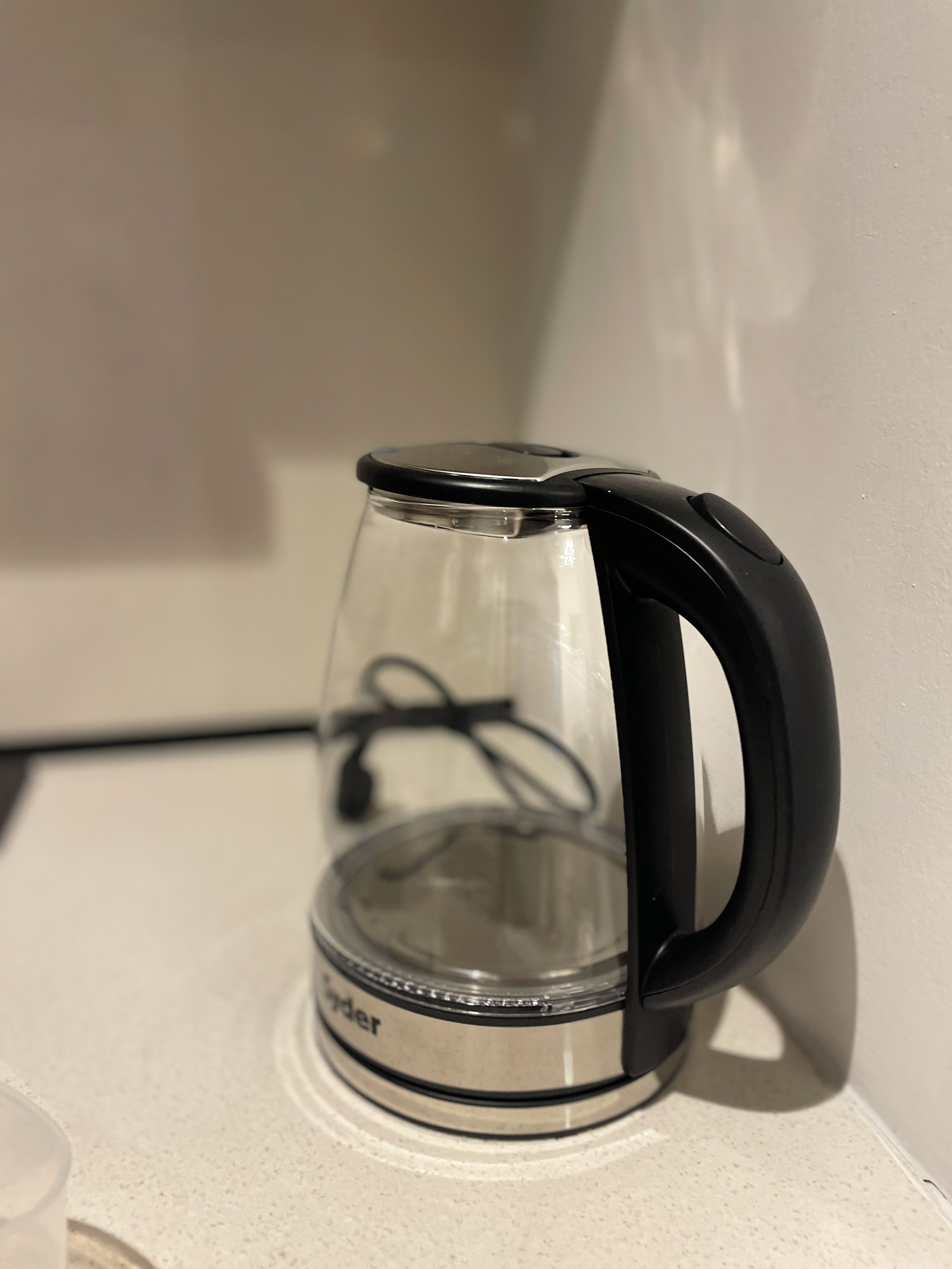 Een transparante elektrische waterkoker met een zwart handvat en voet, geplaatst op een wit aanrecht.