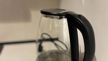 Een transparante elektrische waterkoker met een zwart handvat en voet, geplaatst op een wit aanrecht.