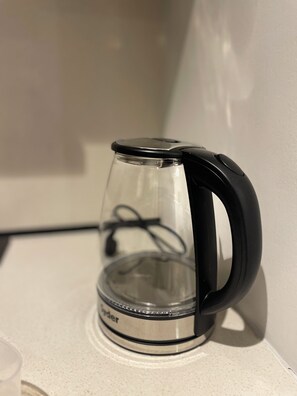 Een transparante elektrische waterkoker met een zwart handvat en voet, geplaatst op een wit aanrecht.