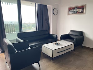 Una sala de estar moderna con un sofá, dos sillones, una mesa de centro y vistas a la ciudad a través de amplios ventanales.