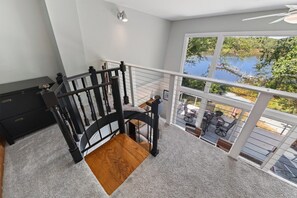 A staircase with a black railing leading to a balcony with a view of a lake and outdoor furniture. - Corrotoman River Retreat - Dock, Kayaks, Shuffleboard & Views (Lancaster)