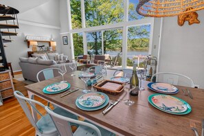 A dining area with a wooden table set for four, surrounded by white chairs. - Corrotoman River Retreat - Dock, Kayaks, Shuffleboard & Views (Lancaster)