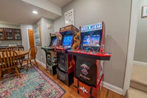 A room with two arcade machines, a dining table with chairs, and a rug. - Corrotoman River Retreat - Dock, Kayaks, Shuffleboard & Views (Lancaster)