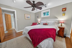 A bedroom with a bed, a ceiling fan, two bedside tables with lamps, a window, and a door. - Corrotoman River Retreat - Dock, Kayaks, Shuffleboard & Views (Lancaster)