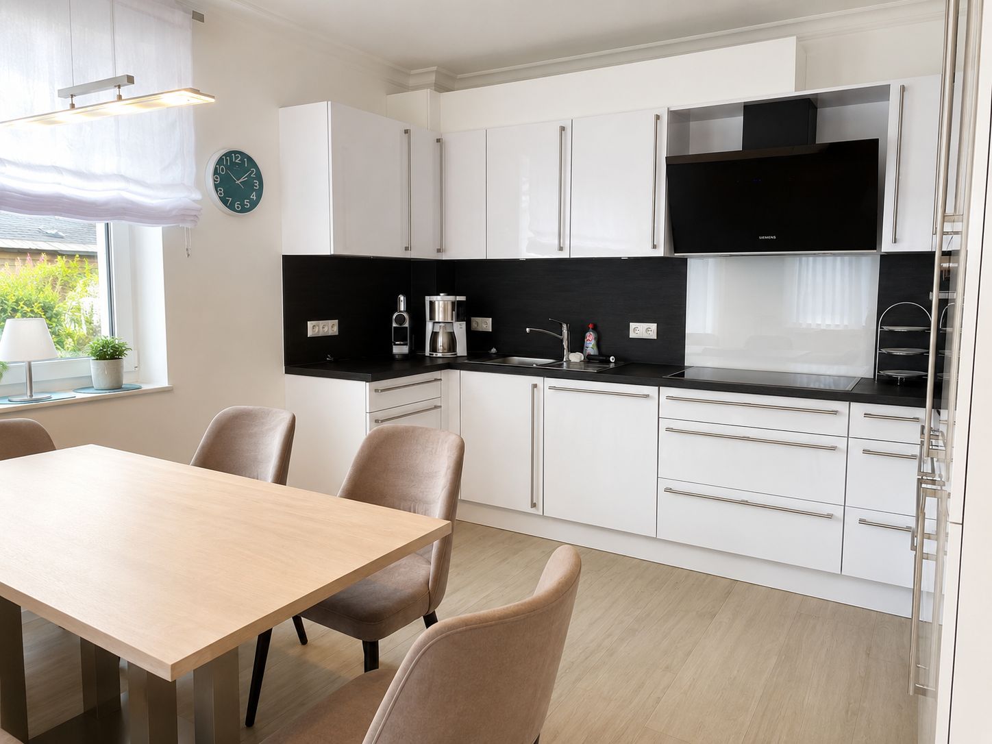 A modern kitchen with white cabinets, a black countertop, and a dining area with a wooden table and chairs.