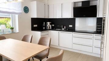 A modern kitchen with white cabinets, a black countertop, and a dining area with a wooden table and chairs.