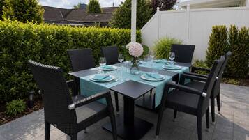 Eine Terrasse im Freien mit einem für sechs Personen gedeckten Tisch, umgeben von Korbstühlen, unter einer weißen Pergola.