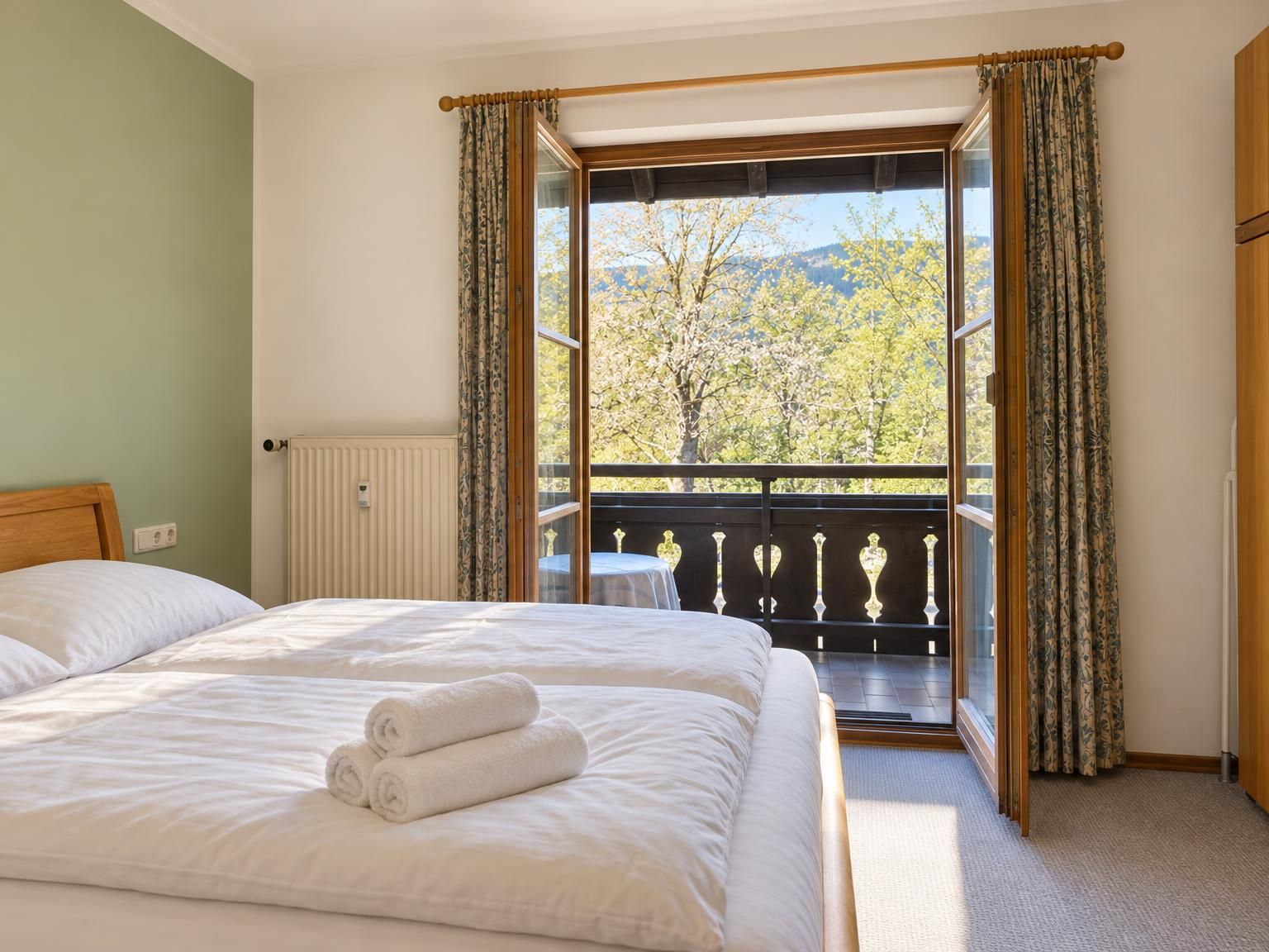 Ein Hotelzimmer mit Bett, einem Fenster mit Vorhängen, einem Heizkörper und Blick auf Bäume und Berge.